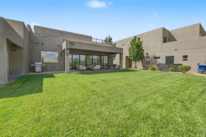 Expansive green lawn, covered patio, large sliding glass doors, upper level balcony, and mature landscaping
