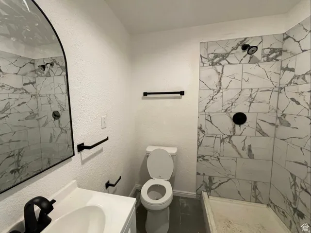 Bathroom featuring a walk-in shower with marble-look tile, matte black shower fixtures, a white vanity with an integrated sink, a matte black faucet, and an arched mirror