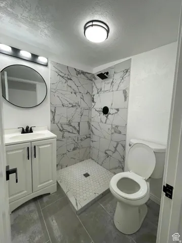 ADU Walk-in shower with large format marble-look tile, hexagonal shower floor tile, single vanity with white cabinetry, matte black hardware, and gray tile flooring