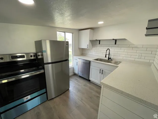 Updated ADU kitchen featuring stainless steel appliances, light countertops, subway tile backsplash, and wood-finish flooring