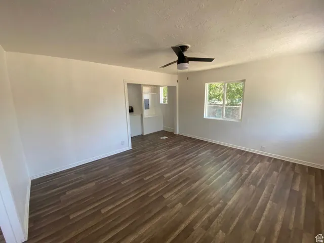 Wood-finish flooring, white walls, ceiling fan with light, and a window providing natural illumination