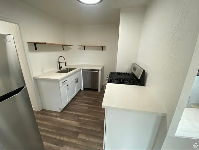 Kitchen featuring wood-finish flooring, white cabinetry with dark hardware, a stainless steel sink with a matte black faucet, and light-toned countertops