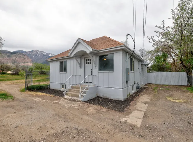 Gabled entry portico with paneled door, light gray vertical siding, and a fenced perimeter