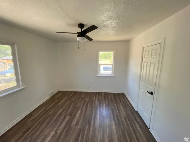 Wood-finish flooring, white walls, two windows with white trim, and a black ceiling fan with an integrated light fixture