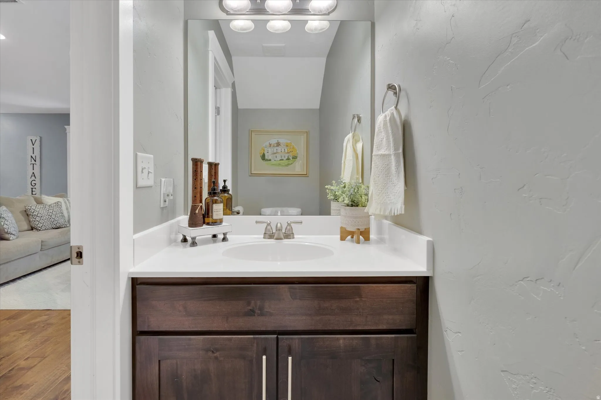 Spa-inspired bathroom vanity featuring a white quartz countertop, dark wood cabinetry with polished chrome hardware, and an illuminated mirror with integrated lighting