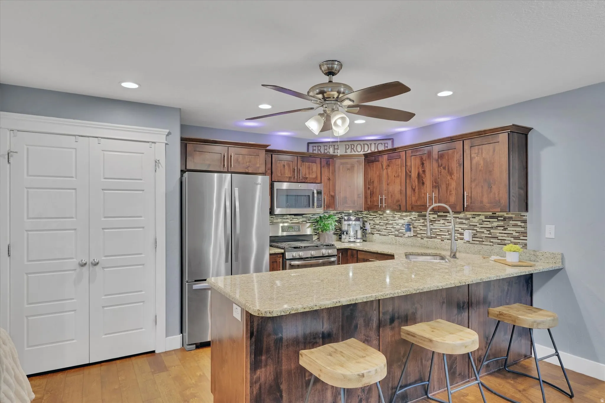 Kitchen featuring stainless steel appliances, wood-finish cabinetry, granite countertops, and a mosaic tile backsplash