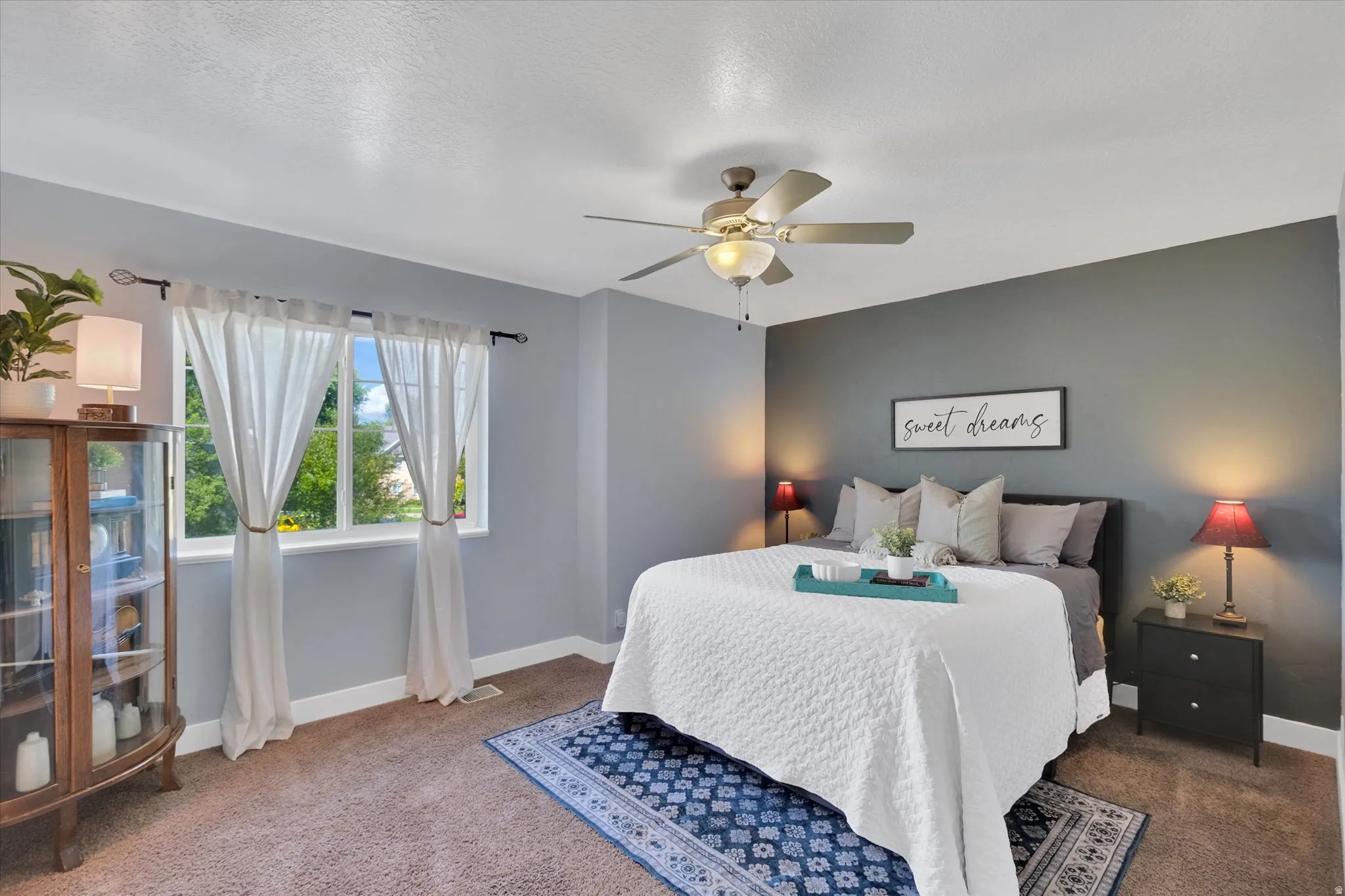 Master bedroom featuring soft blue-gray walls, ceiling fan with integrated lighting, wood-finish flooring, and bedside nightstands with task lighting