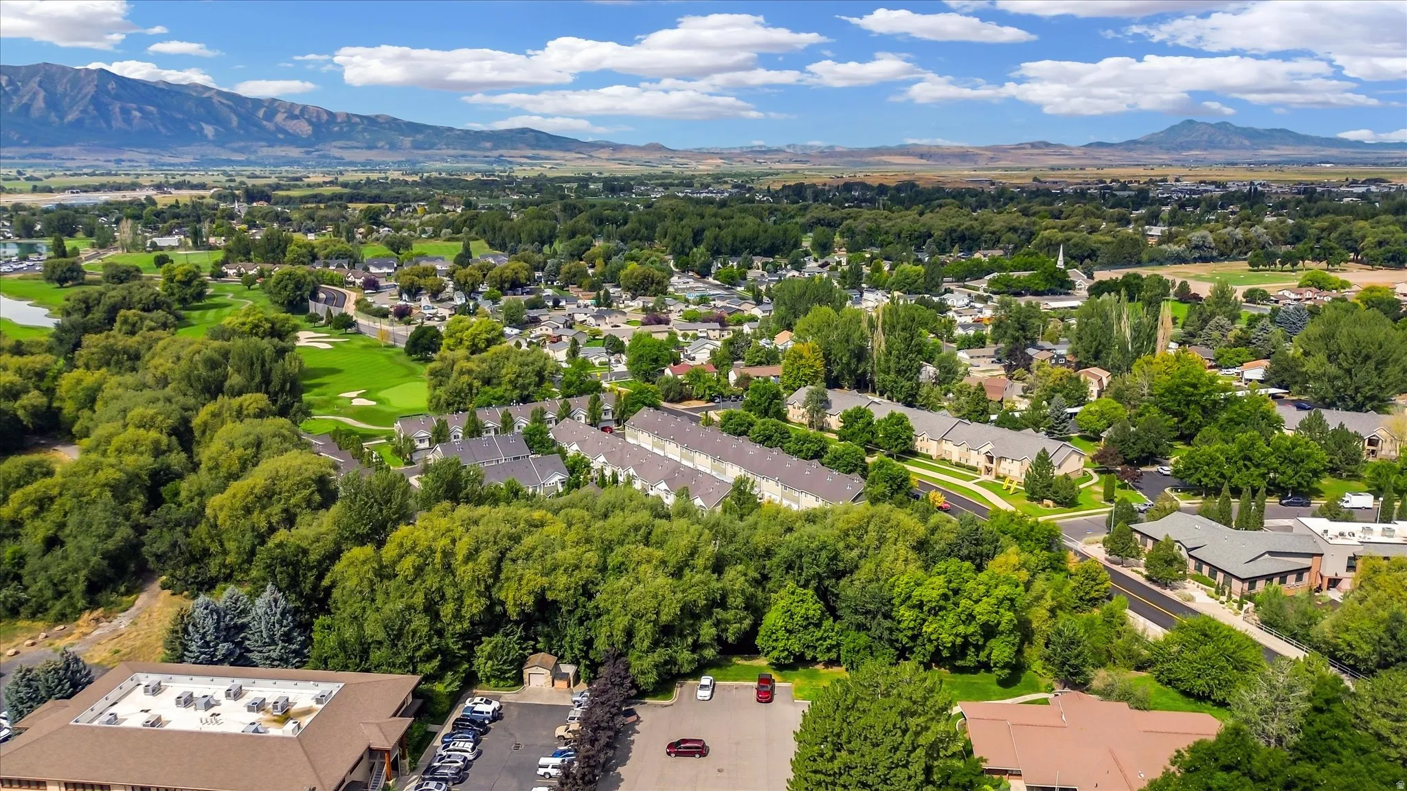 Expansive aerial landscape featuring a golf course, residential areas, mature trees, and distant mountains
