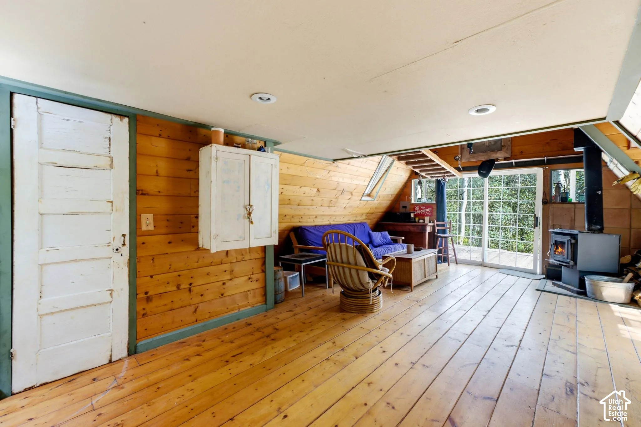 Wood-finish plank flooring, wood-paneled walls, recessed lighting, and a wood-burning stove