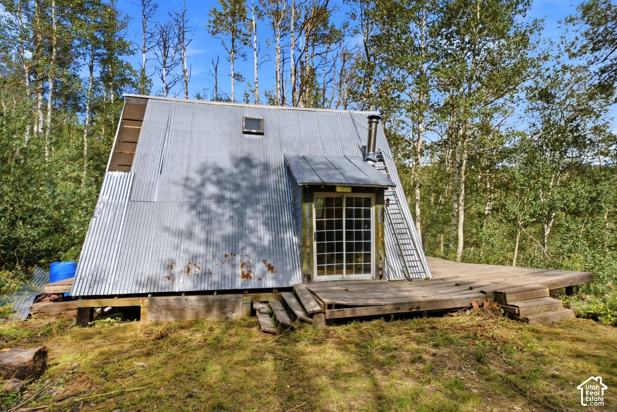 A-frame structure with corrugated metal siding, an integrated deck, and surrounding mature trees