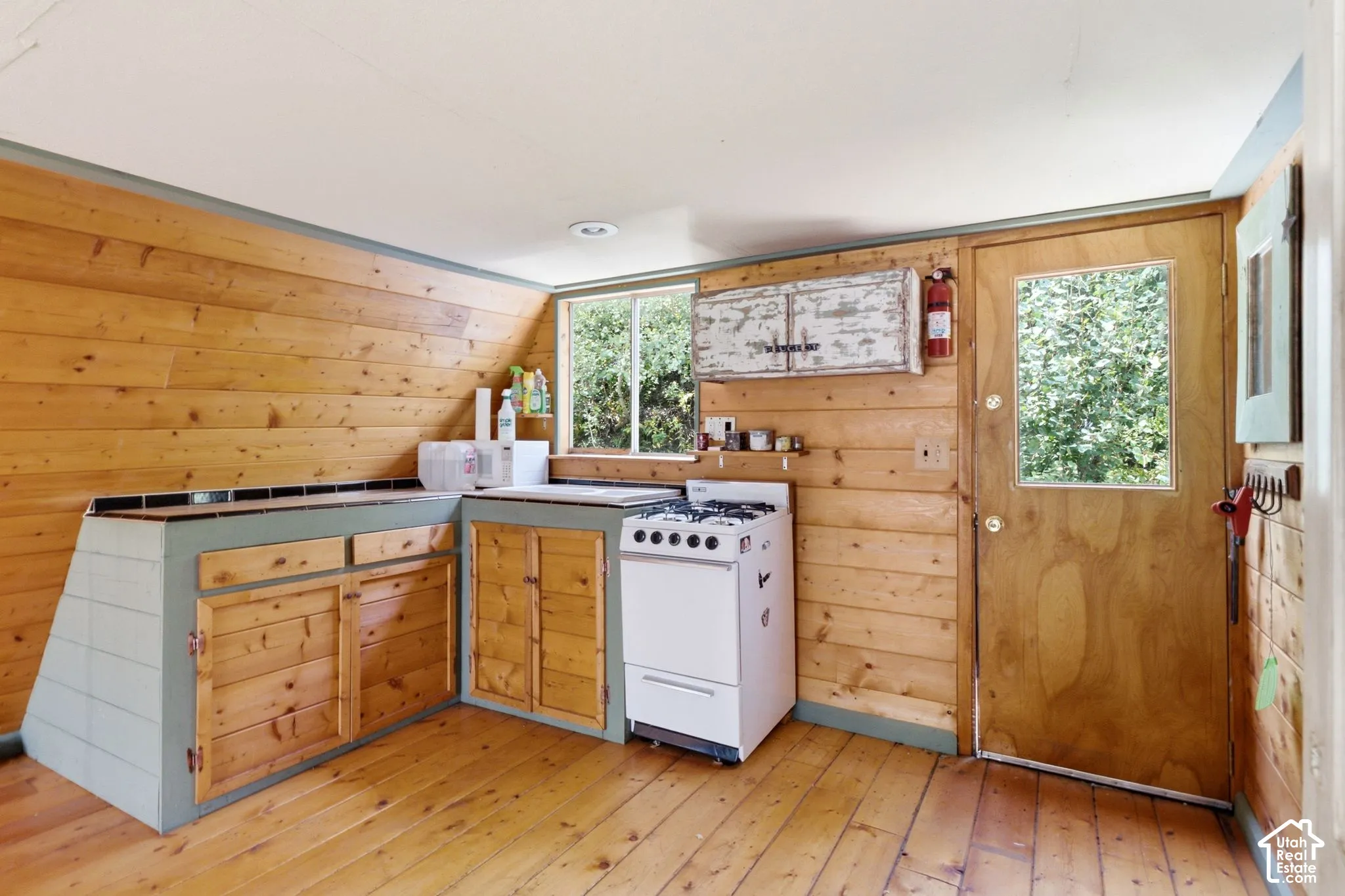 Wood-paneled walls and flooring, built-in cabinetry with wood-front doors, built-in gas range, and a window for natural light