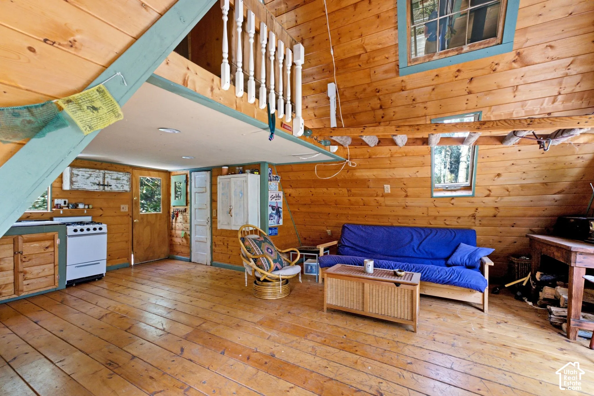 Expansive wood-plank flooring throughout, showcasing natural wood paneling, multiple windows, and a lofted space with baluster railing