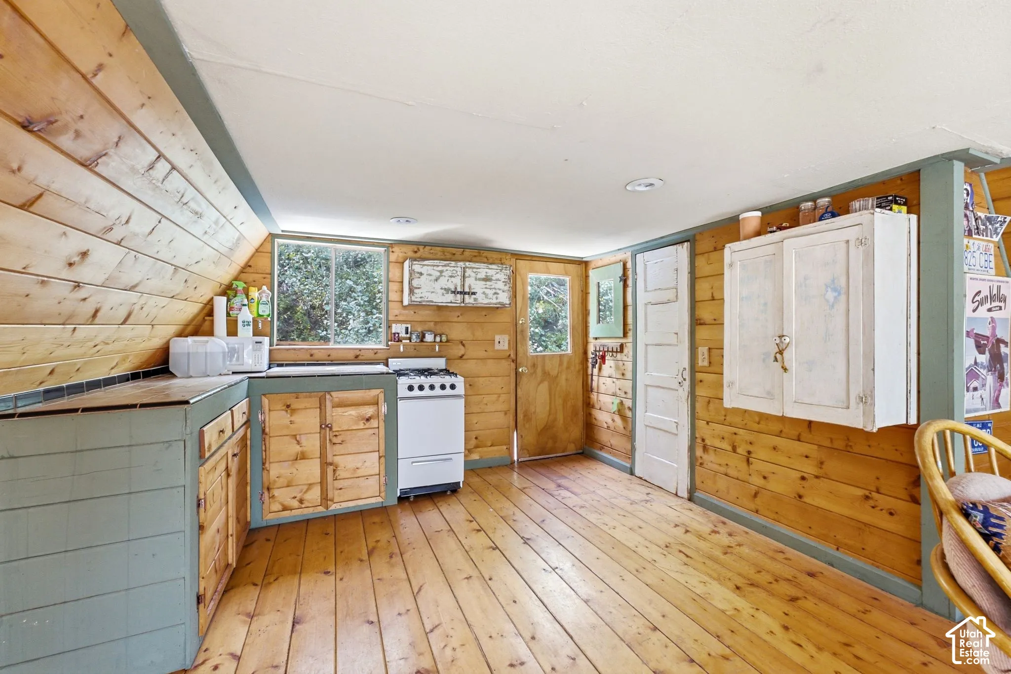 Wood-paneled walls and ceilings, wood-finish flooring, built-in lower cabinetry, a white freestanding range, and a window providing natural light