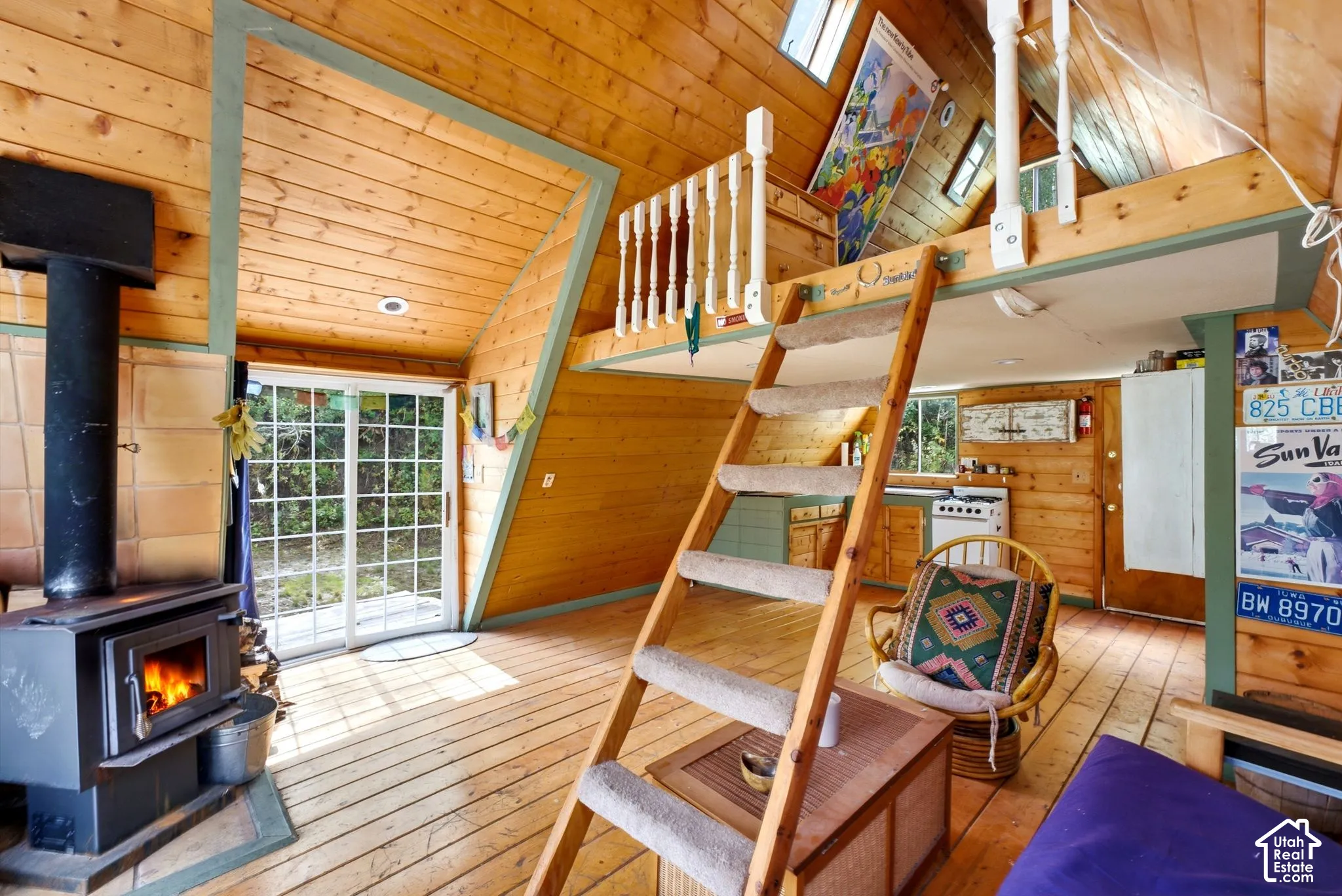 Wood-paneled interior with exposed beams, featuring a wood-burning stove, sliding glass doors, and a built-in ladder accessing a loft space
