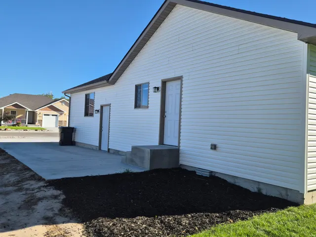 White siding exterior with multiple windows and exterior doors, concrete patio, and landscaped beds
