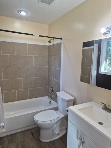 Tub and shower combination with tile surround, wood-finish flooring, recessed lighting, and a vanity with an integrated sink