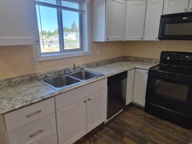 Modern kitchen featuring white shaker-style cabinetry, speckled stone countertops, stainless steel undermount sink with chrome faucet, and black electric range with matching microwave