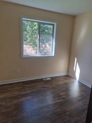 Window with white trim, light-toned walls, and wood-finish flooring