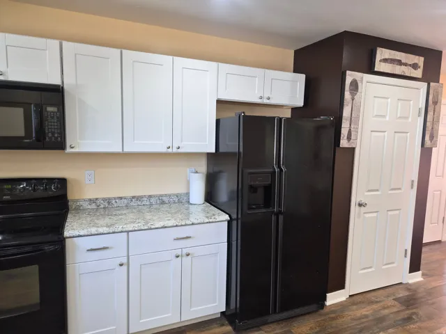 Modern kitchen featuring white cabinetry with brushed hardware, granite-style countertops, and black stainless steel appliances including a side-by-side refrigerator with ice and water dispensers