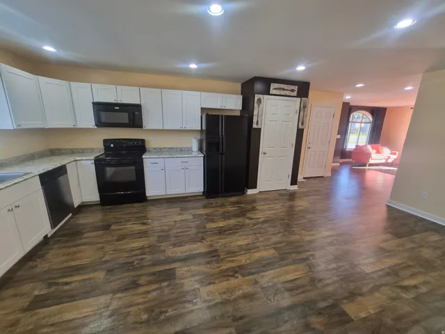 Kitchen featuring white cabinetry, light-toned countertops, black appliances, and wood-finish flooring