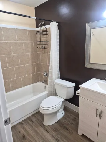 Bathtub with tan subway tile surround, wood-finish flooring, white vanity with integrated sink, and an ornamental framed mirror