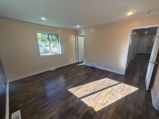 Spacious room featuring wood-finish flooring, recessed lighting, neutral-toned walls, and a large window