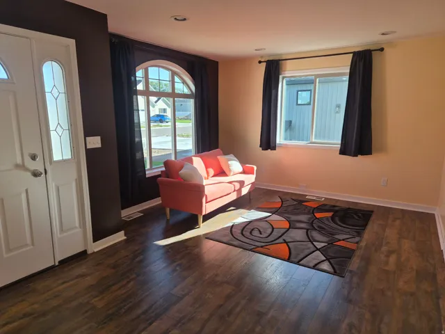 Wood-finish flooring throughout, complemented by a white entry door with decorative glass, and recessed ceiling lighting