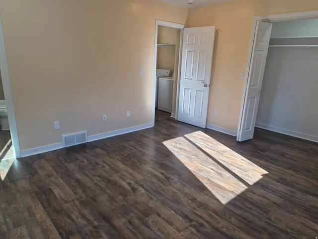 Spacious bedroom with wood-finish flooring, neutral wall finishes, and abundant natural light