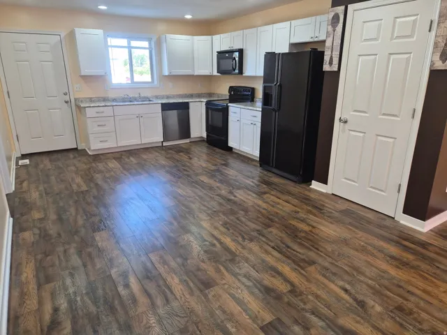 Kitchen featuring wood-finish flooring, white cabinetry, integrated stainless steel dishwasher, black refrigerator, and recessed lighting