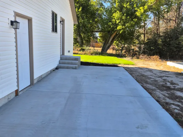 White horizontal siding, concrete patio, concrete steps, exterior wall lanterns, and a rectangular window