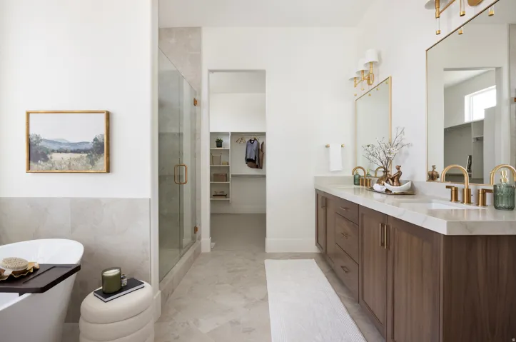 Primary bathroom featuring a wood-finish vanity with dual sinks, white quartz countertops, brass fixtures, and a large framed mirror