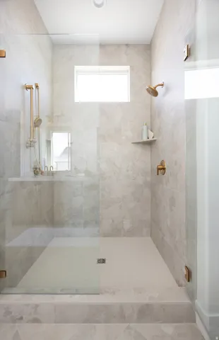 Glass-enclosed shower with a tiled floor, gold-finish fixtures, and a built-in shelf