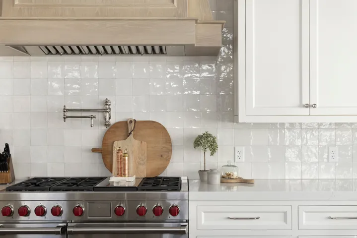 Stainless steel range with red accent knobs, white square-tiled backsplash, and a wall-mounted pot filler