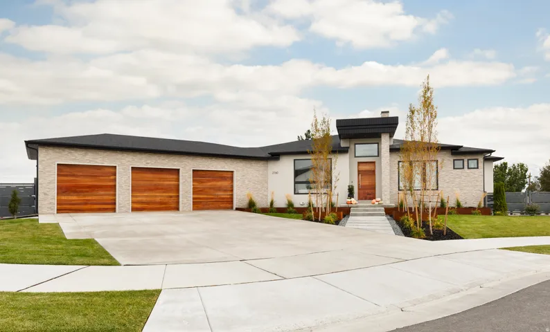 Contemporary exterior design, stone and stucco facade, three wood-finish garage doors, concrete driveway, and a prominent front entry with integrated landscaping