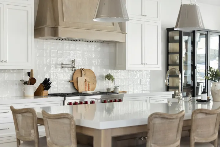 White cabinetry with brushed nickel hardware, natural wood range hood, textured white tile backsplash, professional-grade range, and a large central island with a solid surface countertop