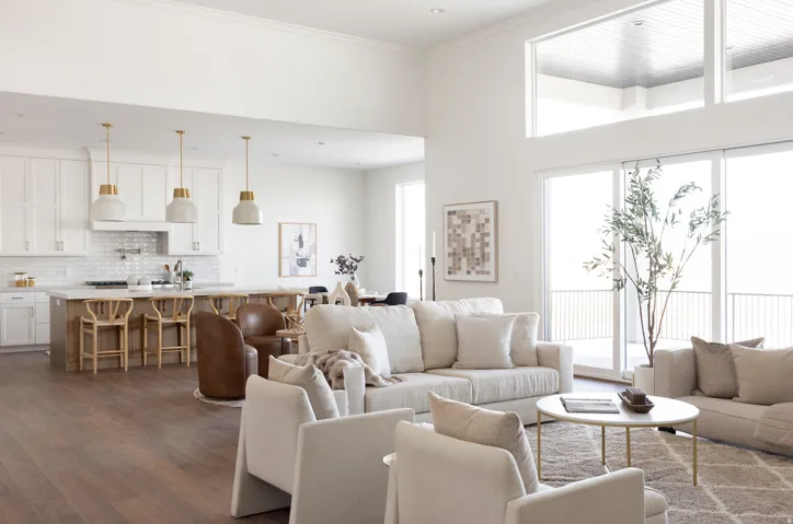Open-concept living space featuring wood-finish flooring, a kitchen island with seating, white cabinetry, and high ceilings