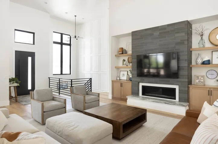 Two-story living area with high ceilings, modern fireplace with tile surround, built-in shelving, and wood-finish flooring