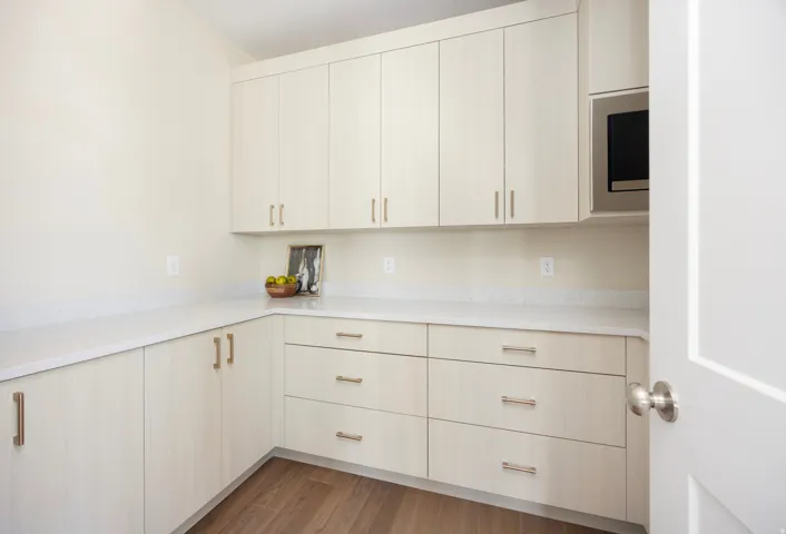 Extensive cabinetry with modern hardware, durable countertops, wood-finish flooring, and a built-in microwave
