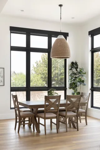 Expansive windows with black trim, wood-finish flooring, recessed ceiling lighting, and a woven pendant light fixture
