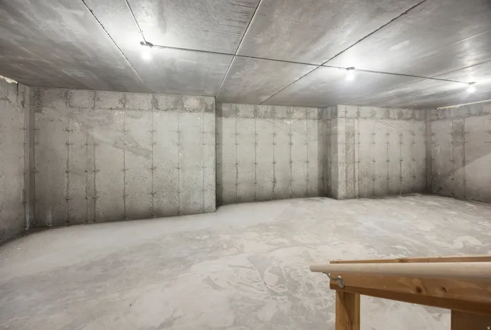 Spacious basement featuring polished concrete flooring, exposed concrete wall panels with integrated reinforcement detailing, recessed ceiling-mounted lighting throughout, and finished ceiling infrastructure ready for customization