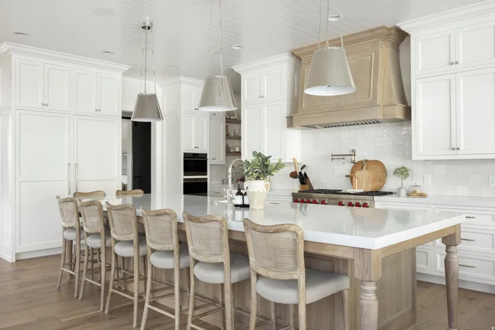 Spacious kitchen featuring an expansive center island with a light-toned wood base, white countertops, extensive white cabinetry, and a light wood-finish range hood