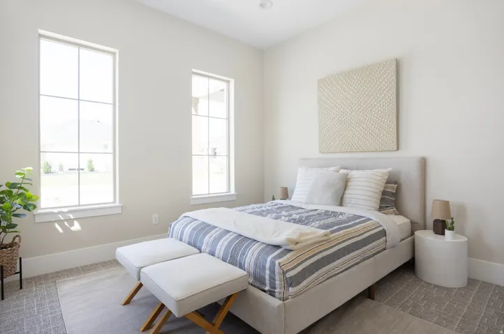 Bright primary bedroom showcasing dual large windows with grid detailing, neutral wall finishes, and light wood-finish flooring