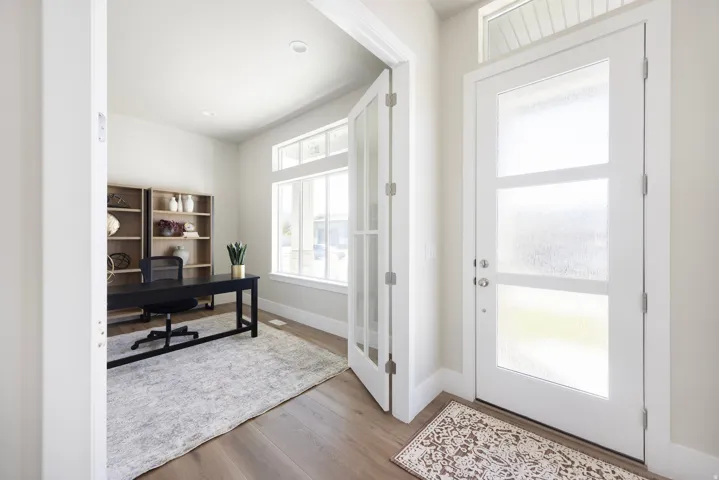 Bright foyer with dual glass-panel doors featuring transom windows and sidelights, hardwood flooring, and generous natural light