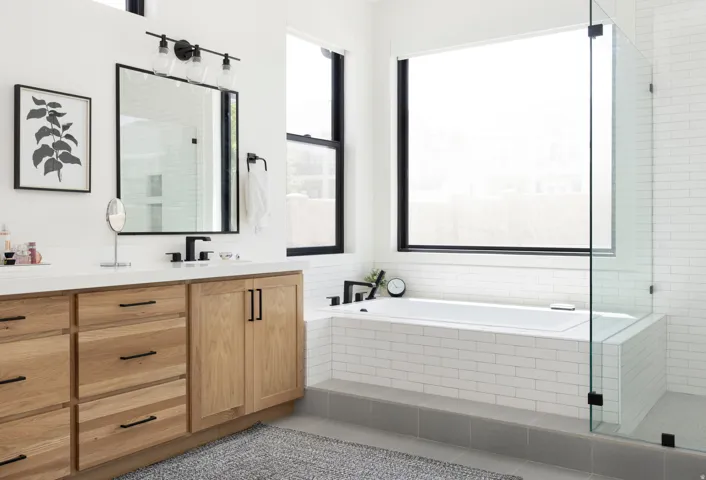 Spa-inspired primary bathroom showcasing a wood-finish vanity with dual sinks, white subway tile surround, and a frameless glass-enclosed soaking tub with integrated shower