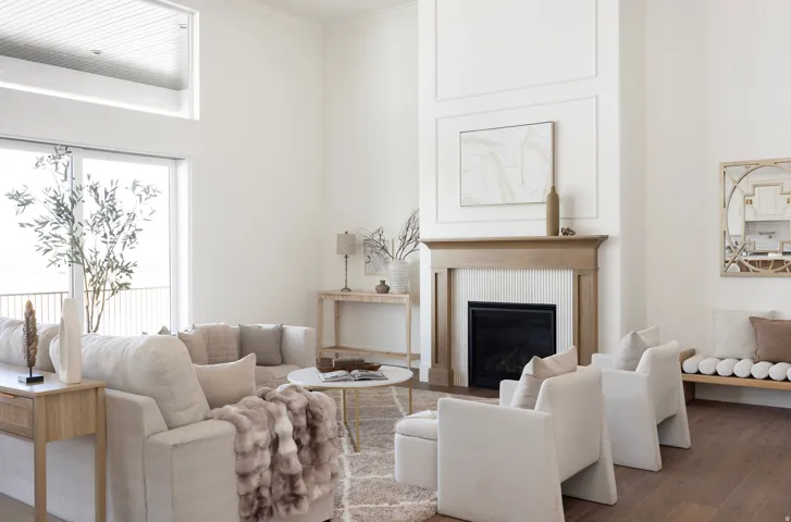 Bright living room anchored by a wood-burning fireplace with a wood-finish mantel, complemented by large windows flooding the space with natural light
