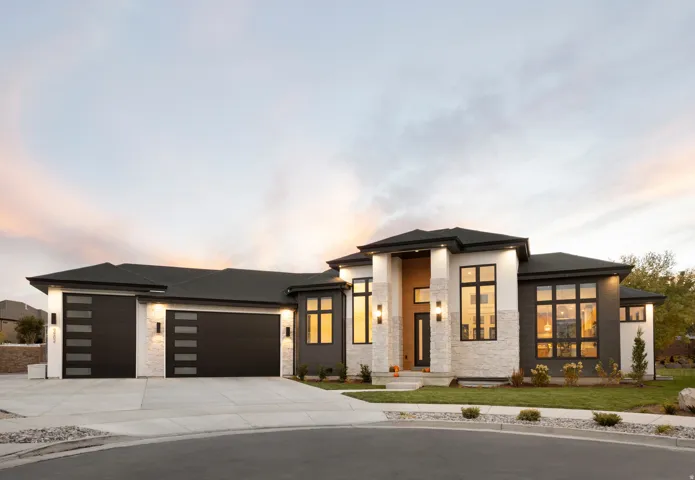 Modern architectural facade featuring stacked stone accents, dark siding, multiple large windows, and a concrete driveway