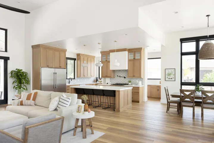 Open-concept living space showcasing natural light through multiple windows, light wood-finish flooring throughout, and a custom kitchen island with seating