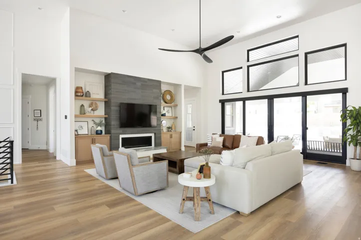 Spacious living area featuring high ceilings, wood-finish flooring, a contemporary fireplace with a dark stone surround, custom built-in shelving, and large sliding glass doors