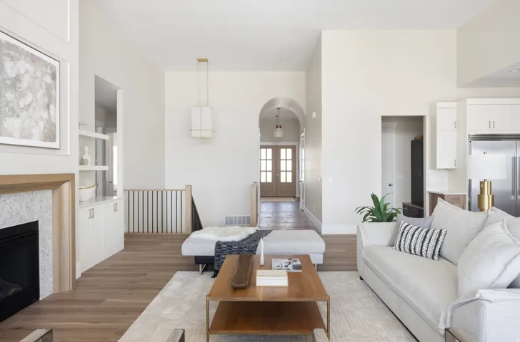 Open-concept living area featuring wood-finish flooring throughout, a two-tier wood coffee table with lower shelf storage, white upholstered seating with striped accent pillows, and a staircase with metal railings
