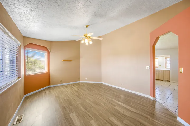 Spacious room featuring wood-finish flooring, multiple windows with blinds, a ceiling fan, and an arched doorway